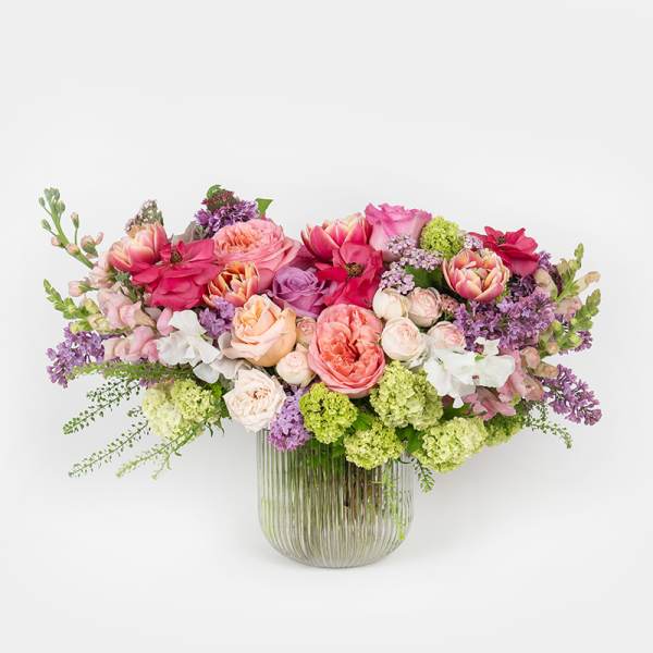 Low arrangement of pink, peach, and purple flowers in a ribbed clear glass vase