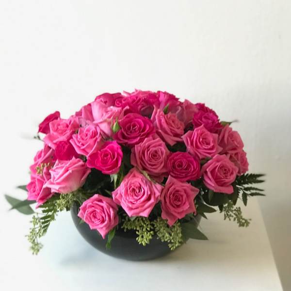 Low round arrangement of hot pink roses in a black bowl-shaped vase