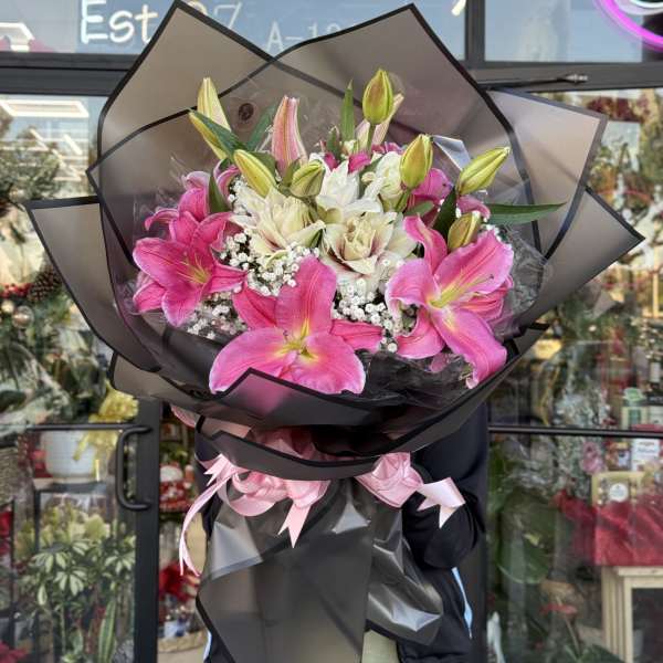Large bouquet of pink and white lilies with baby's breath wrapped in black paper with pink ribbons