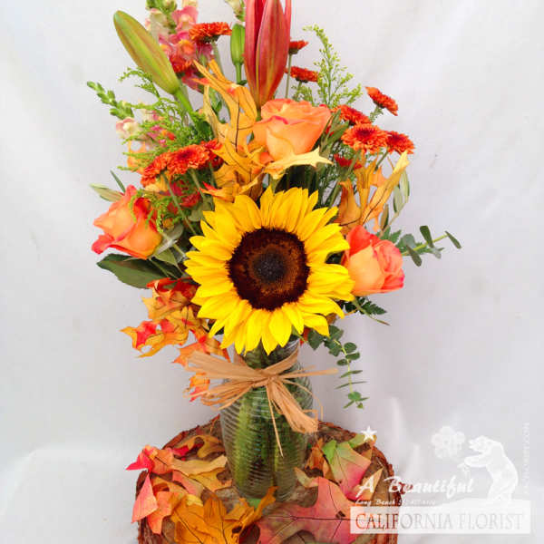 Sunflower and orange rose arrangement in a glass vase with autumn leaves