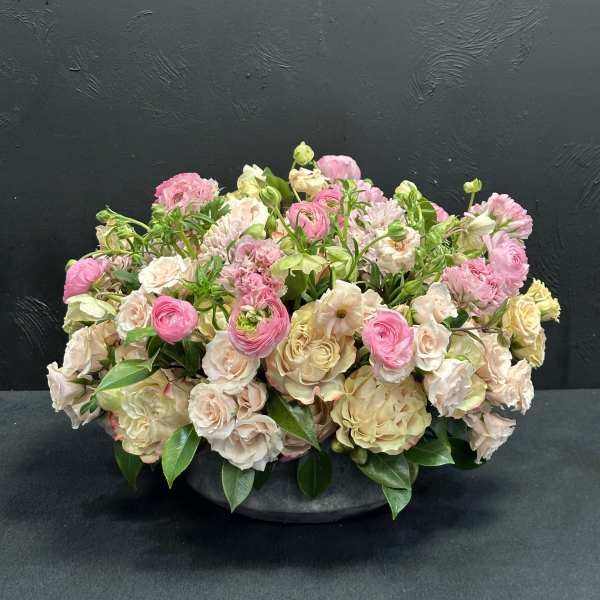 Low arrangement of pink and cream flowers in a dark bowl