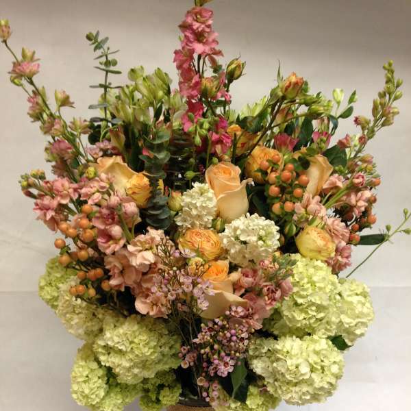 Tall mixed bouquet in a burlap-wrapped vase with peach, pink, and green blooms