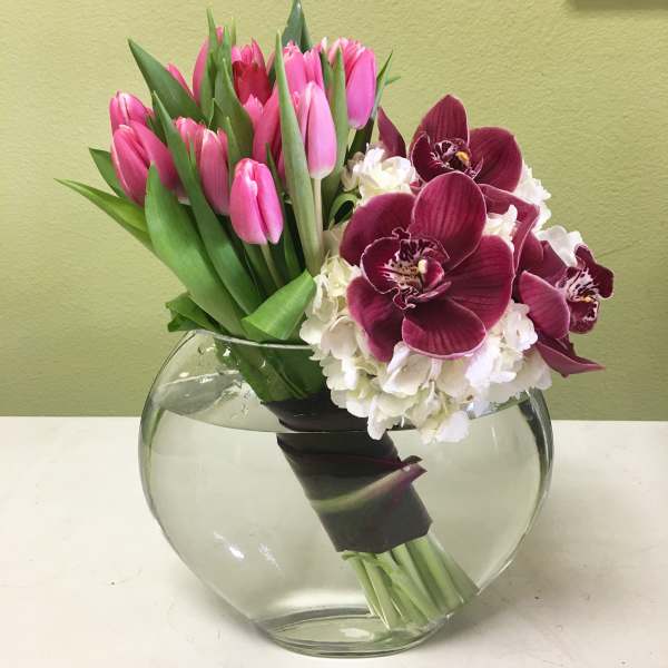 Pink tulips and burgundy orchids in a round glass vase