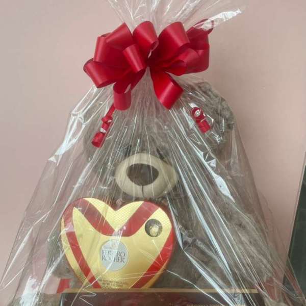 Gift basket with teddy bear and heart-shaped chocolate box wrapped in clear cellophane