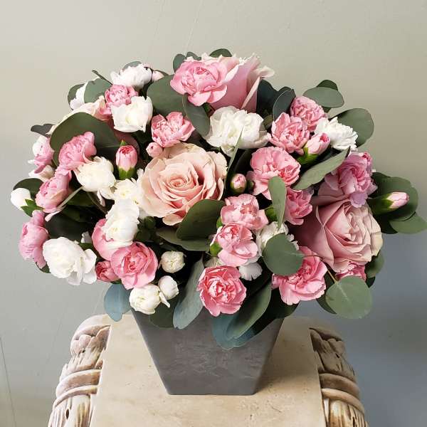 Pink and white roses and carnations arranged in a gray square vase