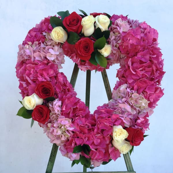 Heart-shaped floral wreath of pink hydrangeas and red and white roses on a stand