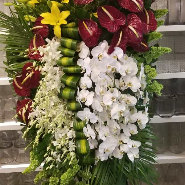 Tall standing floral spray with yellow lilies, burgundy anthuriums, and white orchids
