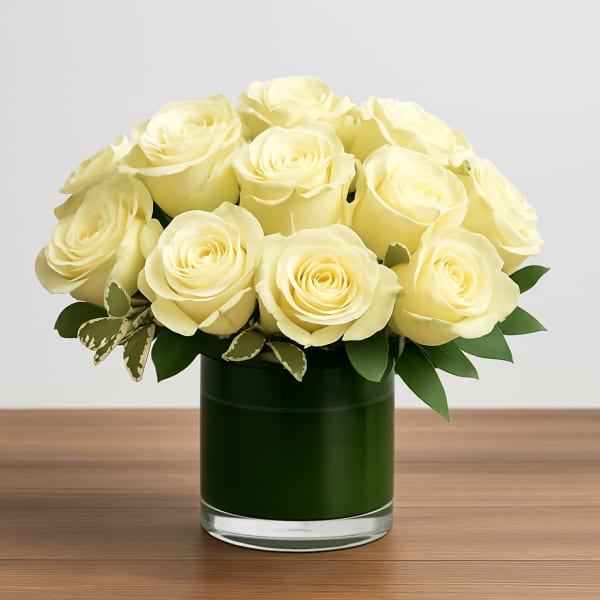 Short glass vase of pale yellow roses arranged in a tight, rounded cluster