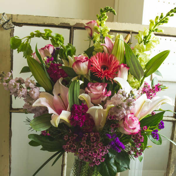 Mixed bouquet of lilies, roses, and purple flowers in a glass vase