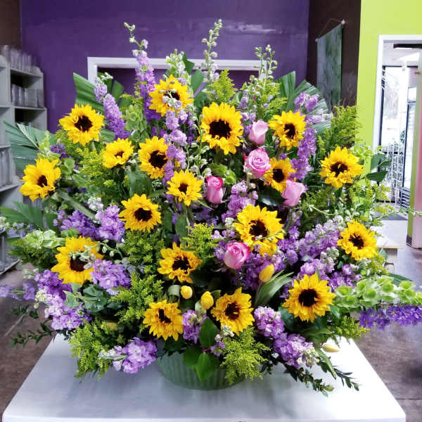 Large arrangement of yellow sunflowers, pink roses, and purple flowers in a green container