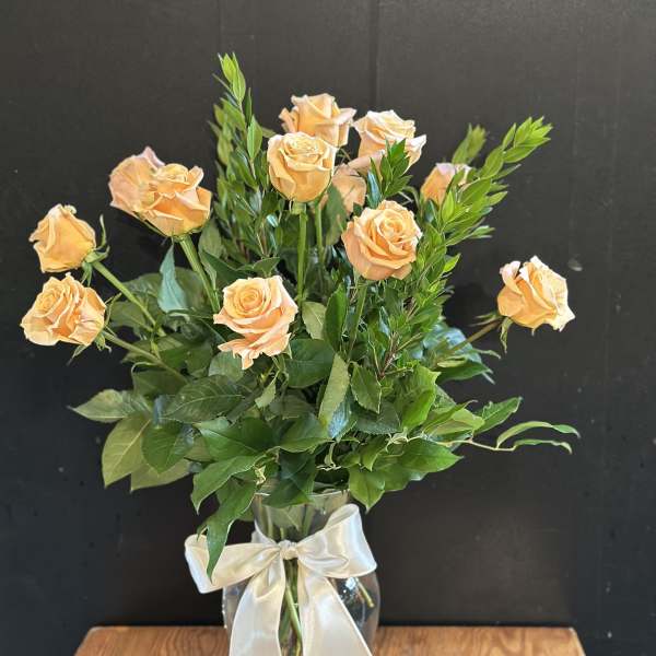 Peach roses arranged in a clear glass vase with a white ribbon.