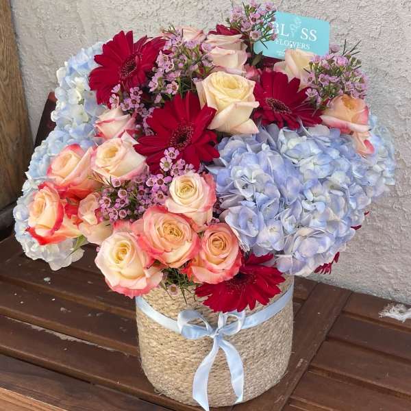 Bouquet of roses, gerbera daisies, and hydrangeas in a woven basket