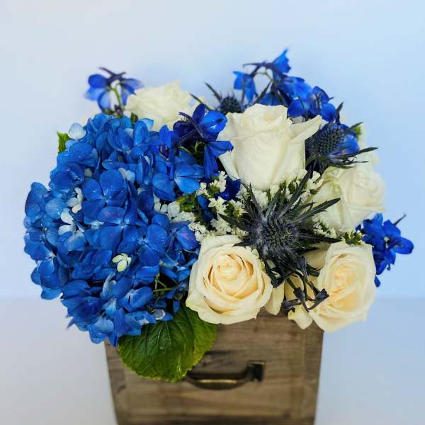 Blue hydrangeas and white roses arranged in a wooden box
