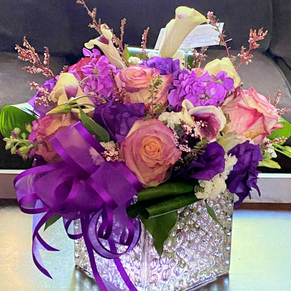 Purple and pink floral arrangement in a clear textured cube vase