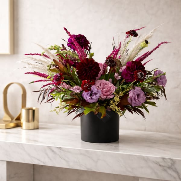 Mixed bouquet of pink, purple, and burgundy flowers in a black vase