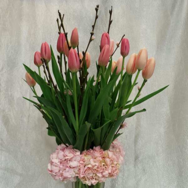 Pink tulips and pale pink hydrangeas in a tall glass vase
