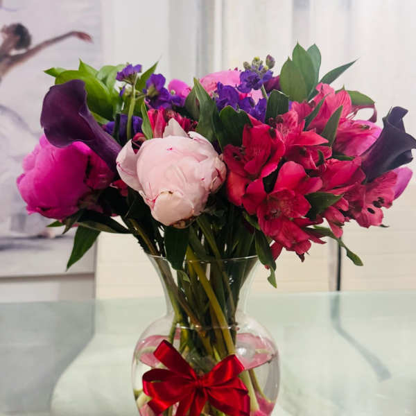 Pink and purple bouquet in a clear vase with a red ribbon