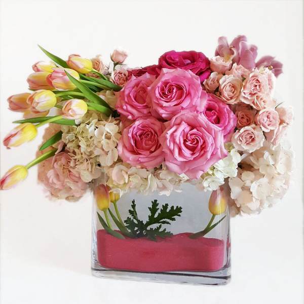 Pink roses and tulips arranged in a clear rectangular vase