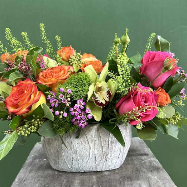 Mixed roses and orchids arranged in a white textured vase