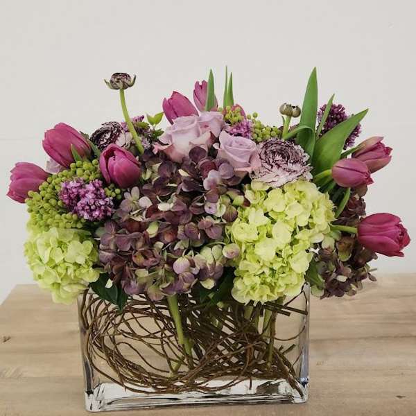 Low rectangular vase with purple tulips, hydrangeas, roses and ranunculus in purple and green tones