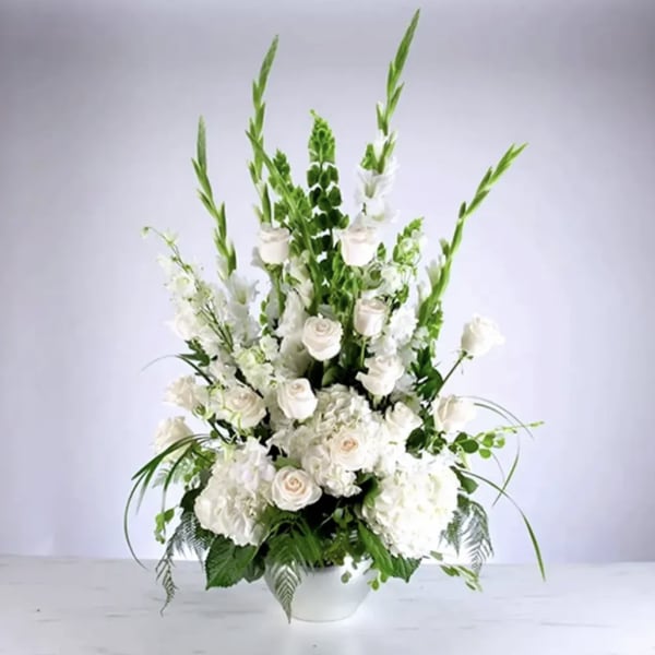 Tall white floral arrangement in a white vase with roses and lilies