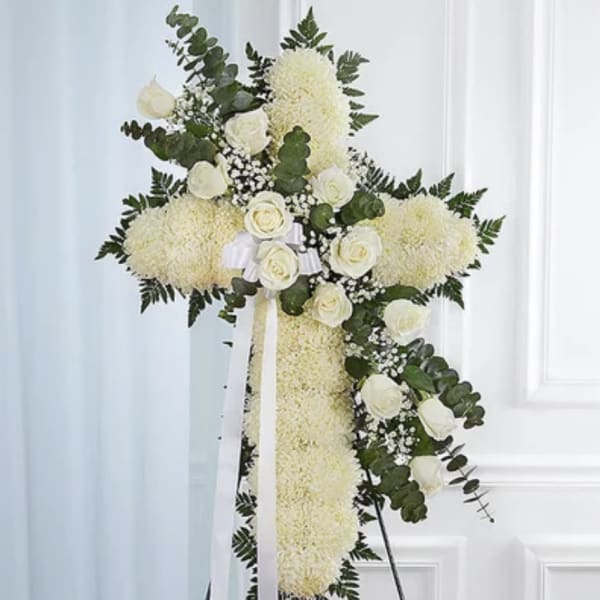 Standing cross of white flowers with white roses and ribbon on an easel