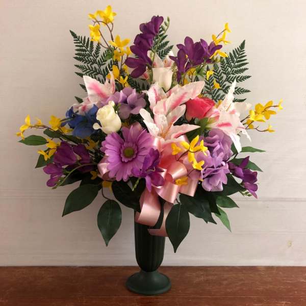 Tall mixed arrangement of lilies, roses, and purple daisy in a dark pedestal vase with pink bow