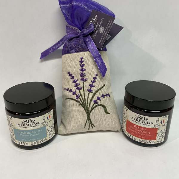Two scented candles flank a lavender sachet gift bag.