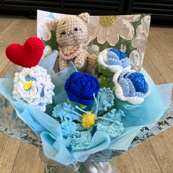 Crocheted blue and white flower bouquet with a small crocheted cat and red heart in a glass vase.