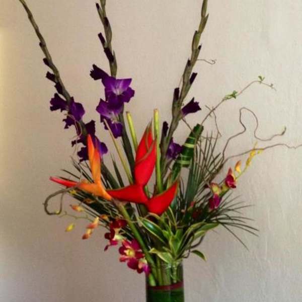 Tall tropical arrangement with red and orange bird-of-paradise and purple orchids in a vase