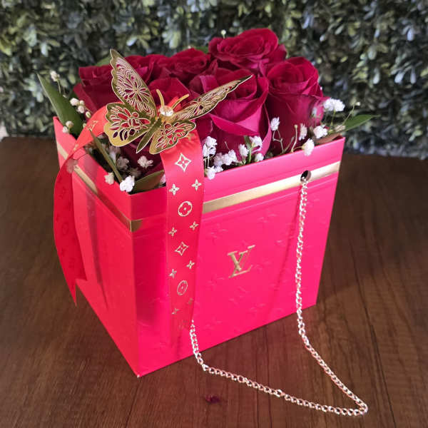 Pink box arrangement of red roses with a ribbon and butterfly decoration