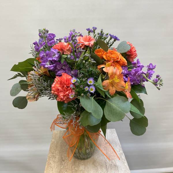 Mixed bouquet of purple, orange, and coral flowers in a glass vase