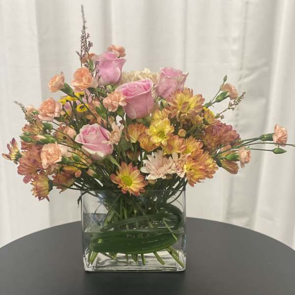 Pink roses and mixed blooms in a clear square vase