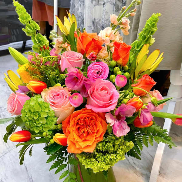 Bright mixed bouquet of pink, orange, and green flowers in a clear glass vase