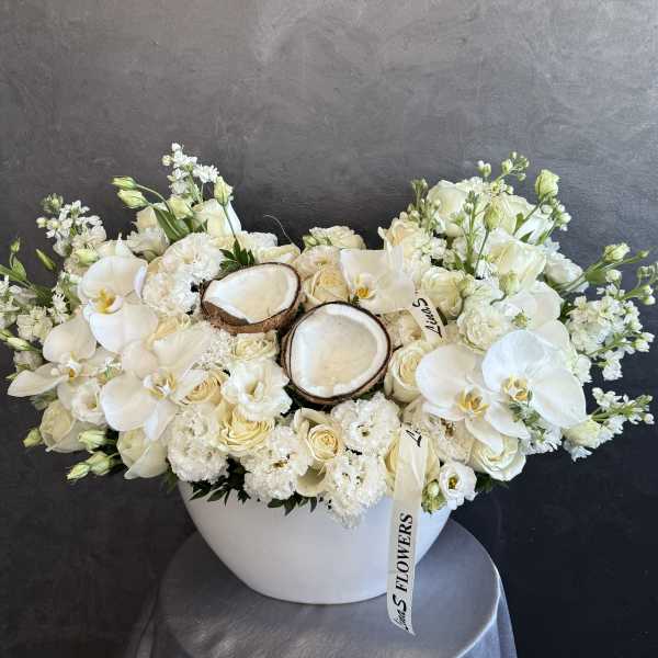 White floral arrangement with orchids, roses, and coconut halves in a white bowl