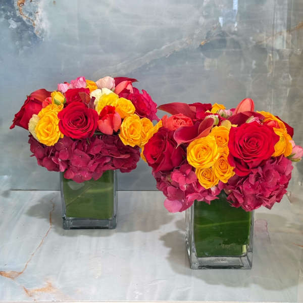 Two colorful rose arrangements in square glass vases