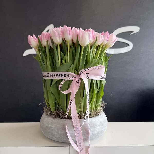 Pink tulips arranged in a round gray planter with a pink ribbon