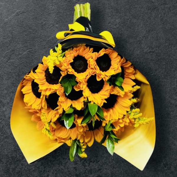 Bouquet of bright yellow sunflowers with green accents wrapped in yellow paper and black ribbon