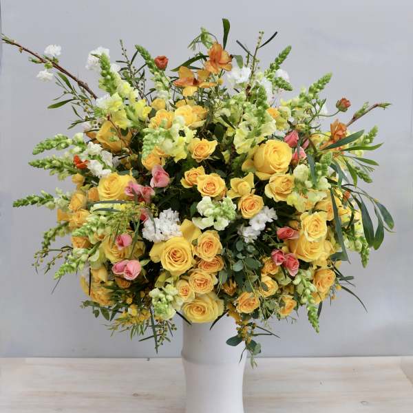 Tall arrangement of yellow roses with white and pink flowers in a white vase