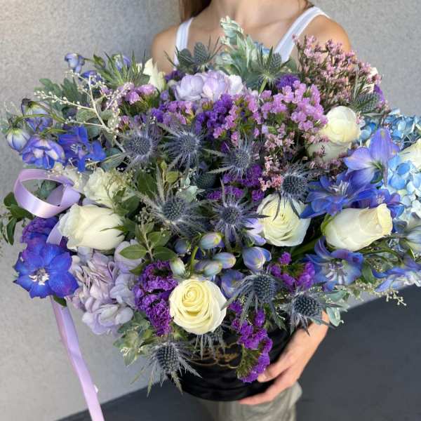 Large bouquet of blue, purple, and white flowers with a lavender ribbon