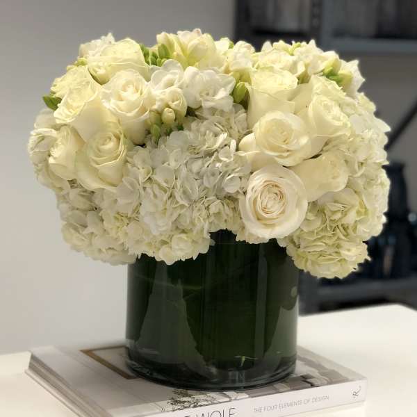 Low round arrangement of white roses and hydrangeas in a glass cylinder vase