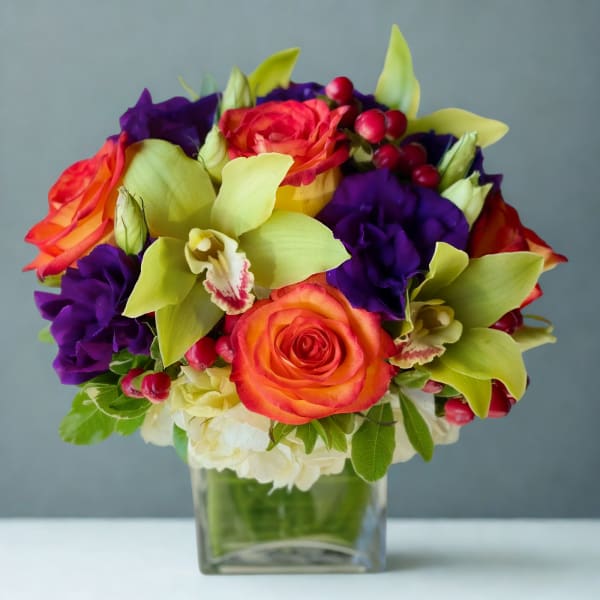 Colorful bouquet of roses and orchids in a clear square vase