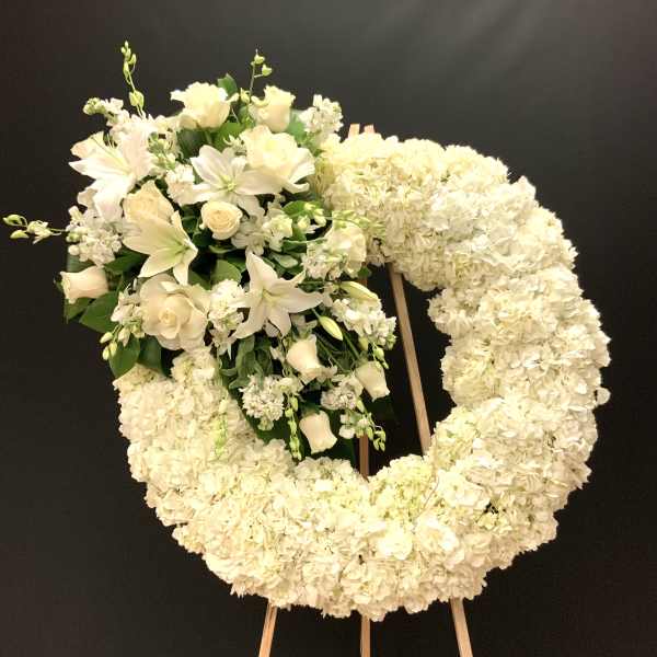 White floral wreath on an easel with a cluster of lilies and roses