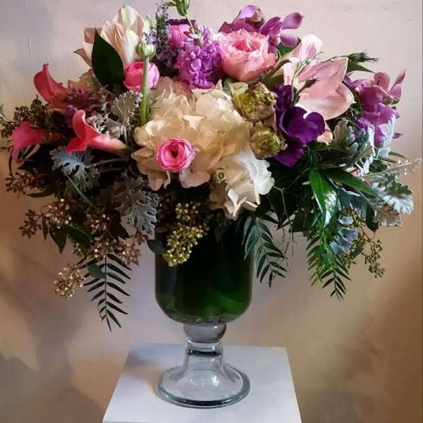 Mixed pink and purple flower arrangement in a green glass vase