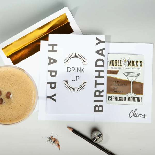 Birthday card reading Drink Up with gold-lined envelope and espresso martini drink mix packet.