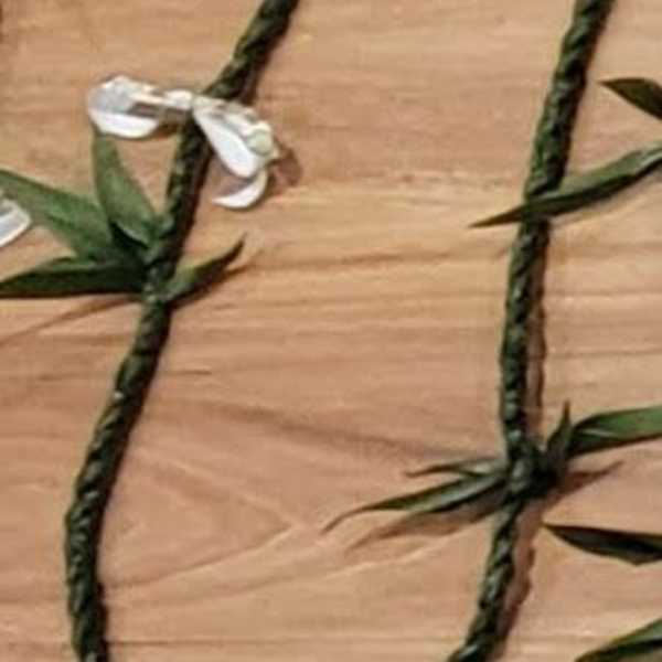 Braided green floral garland with small white blossoms on a wood surface