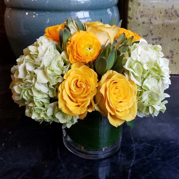 Yellow roses and white hydrangeas arranged in a glass vase