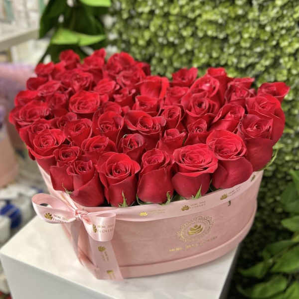 Heart-shaped pink box filled with tightly packed red roses and tied with a matching ribbon.
