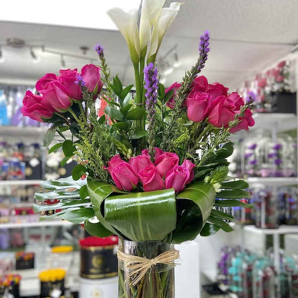 Tall arrangement of hot pink roses and white calla lilies in a clear glass vase with a collar of broad green leaves