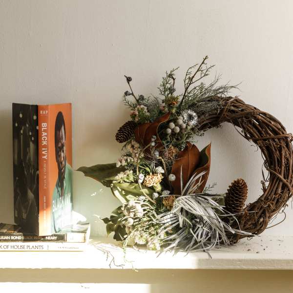 Rustic wreath with pinecones and dried florals beside stacked books